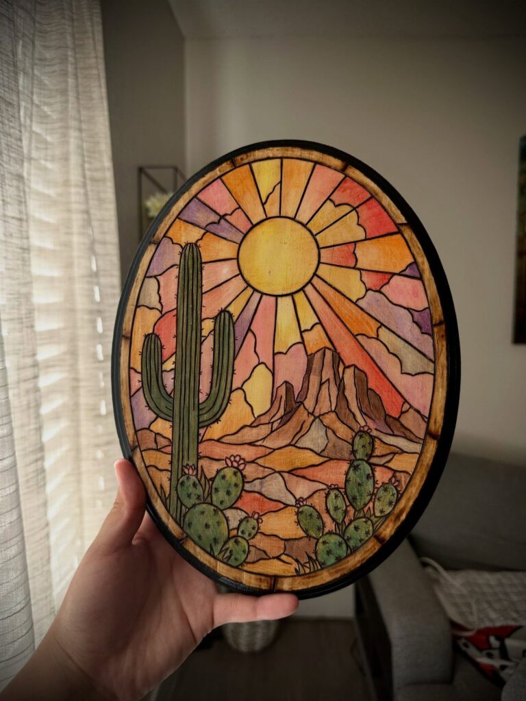 Circular wooden plaque with colorful stained desert landscape and burnt wood outlines.