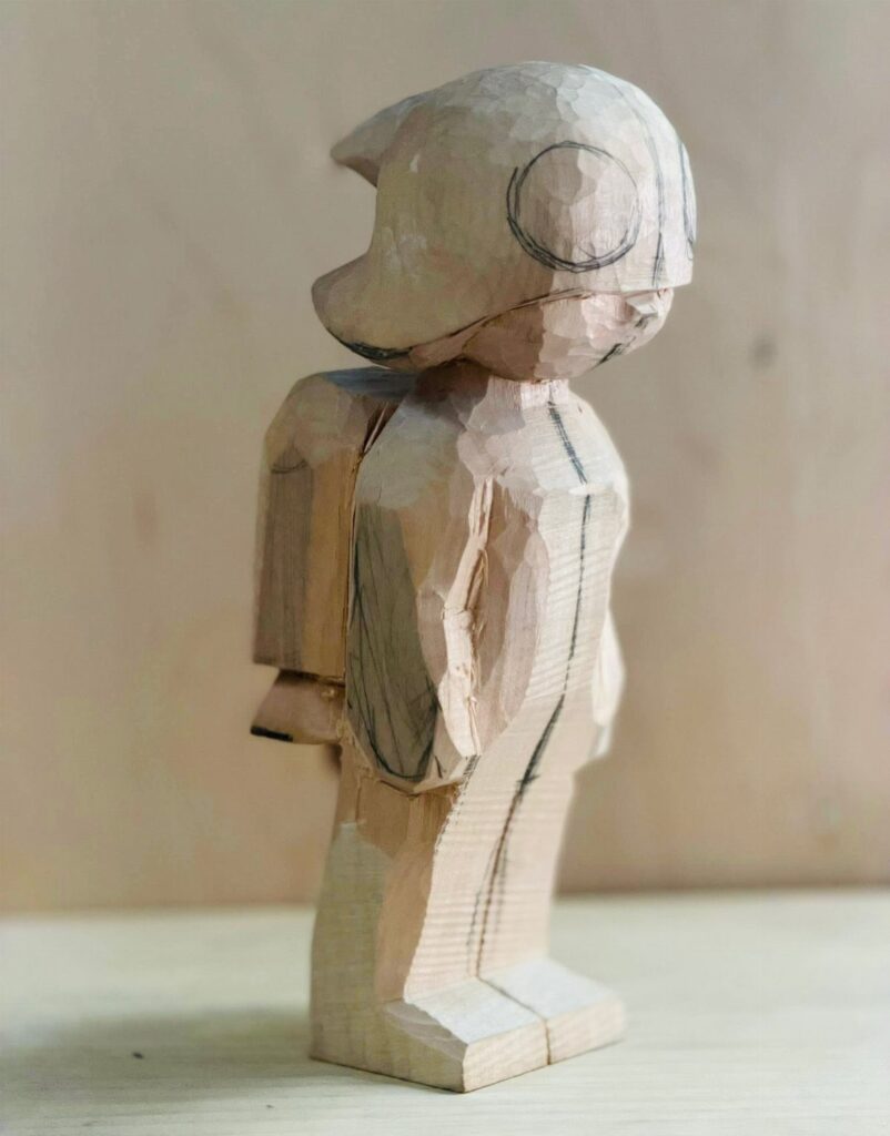 Hand-carved wooden figure of a person with a helmet and backpack.