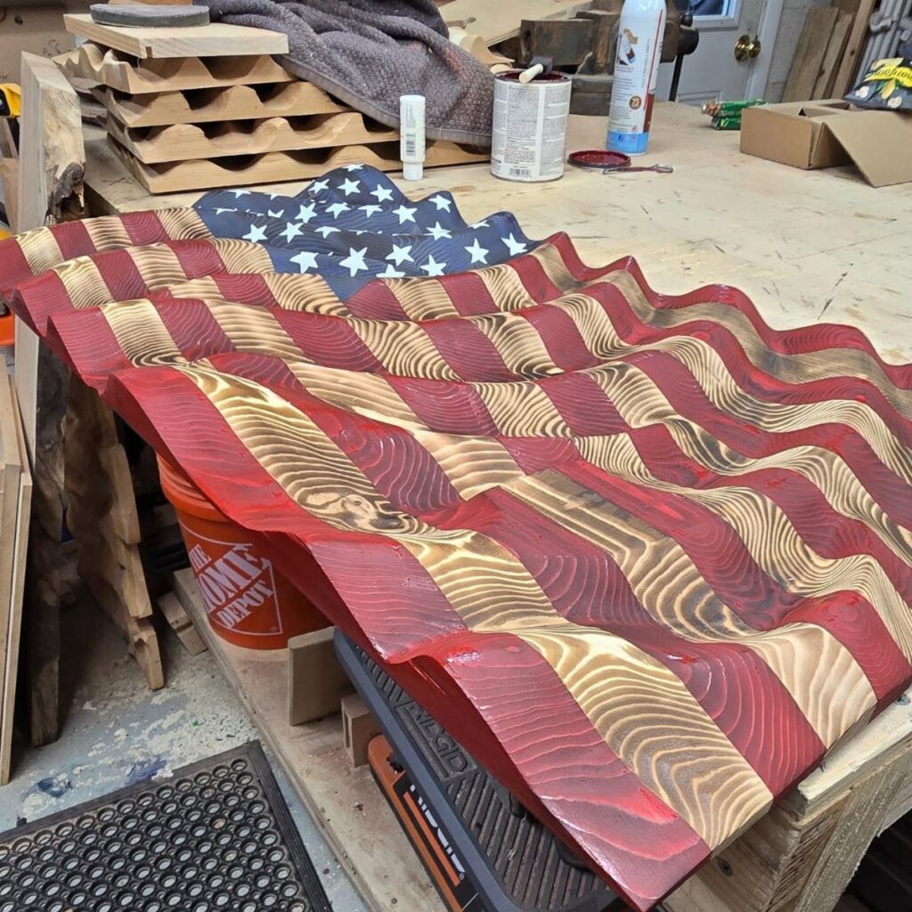 Carved wooden American flag with wavy 3D stripes resting on a workshop table.