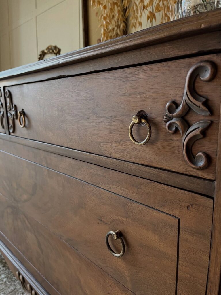 Dark brown wooden dresser with ornate carvings and brass ring drawer pulls