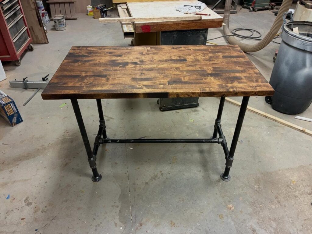 Wooden desk with a black industrial pipe and fittings frame in a workshop.
