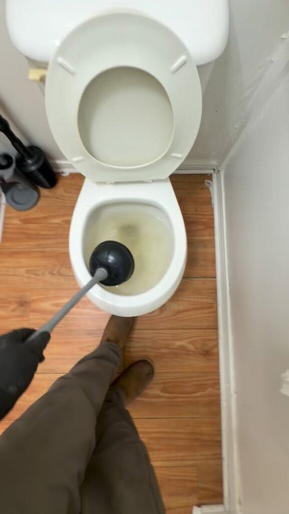 Person using a black plunger to unclog a white toilet bowl with water.