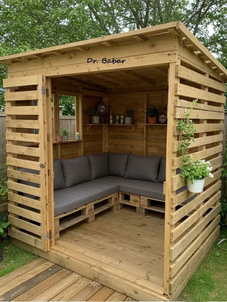 Wooden pallet gazebo with grey corner seating and potted plants in a garden