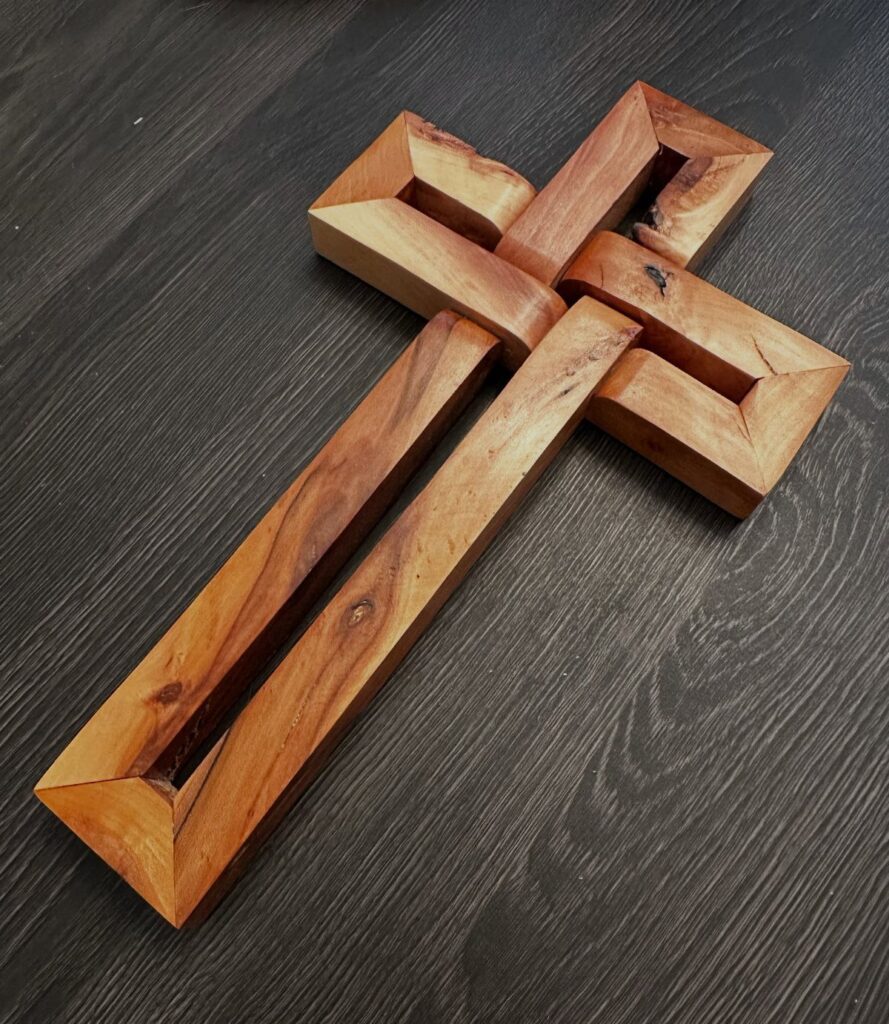 Wooden woven infinity cross made of light brown wood on a dark surface