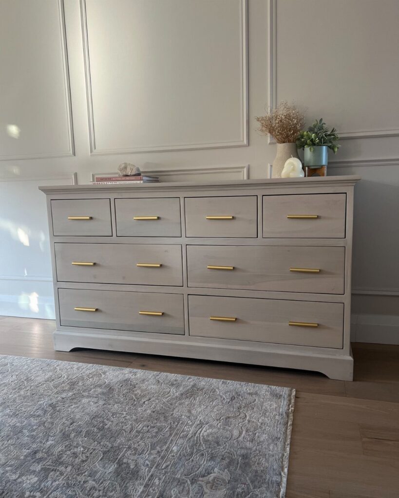 Grey painted dresser with modern gold bar handles against a paneled wall.