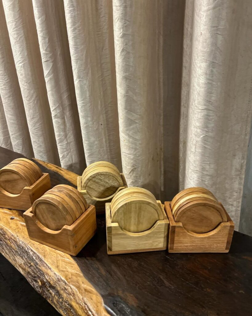 Circular wooden coasters in square wooden holders on a dark live-edge table.