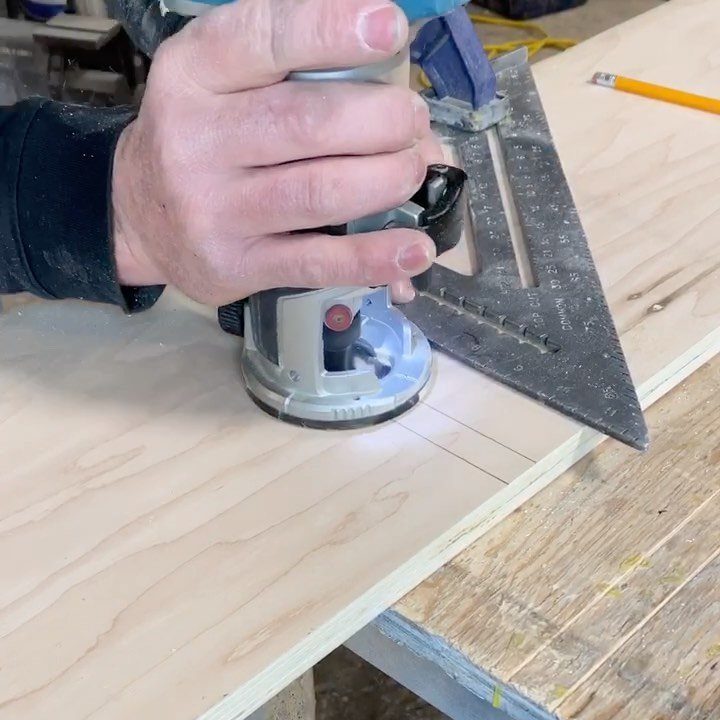 Hand using a power router and speed square to cut a groove in plywood.