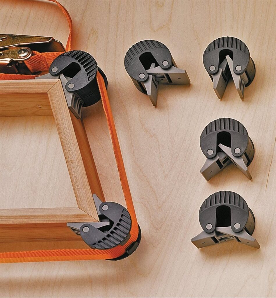 Right-angle clamps securing the mitered corners of a light wooden picture frame.