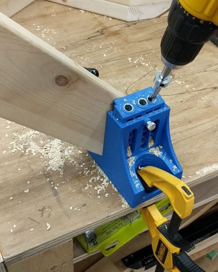 Power drill driving a screw into wooden boards using a blue pocket-hole jig.