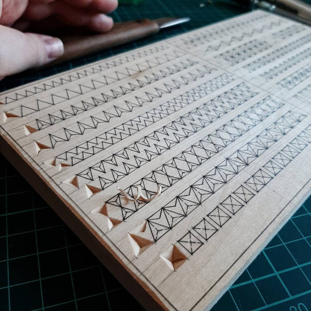 Wooden board with geometric chip carving patterns being carved by a hand tool.