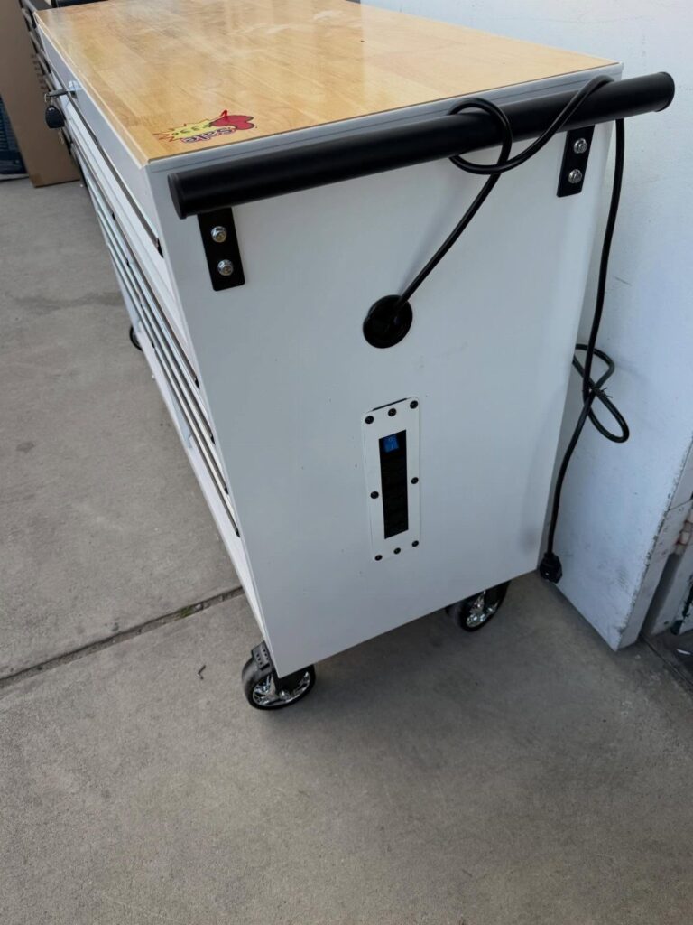 White mobile tool cabinet with wooden top and black caster wheels in a garage.