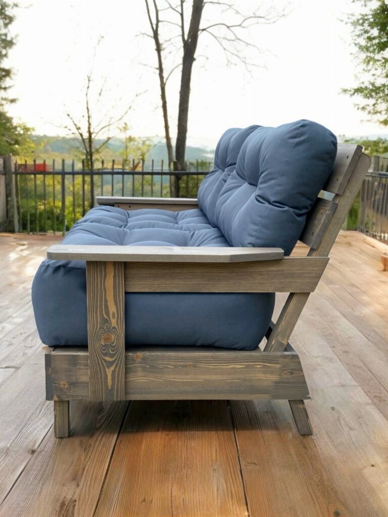 Grey wooden outdoor couch with blue cushions on a sunny wooden deck.