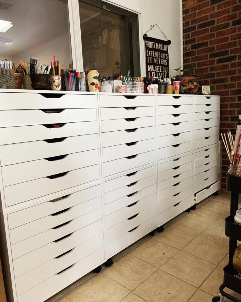 White multi-drawer storage cabinet filled with art supplies and paintbrushes in a studio.