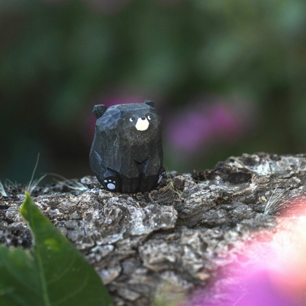 Small black wooden bear carving sitting on a piece of rough tree bark.