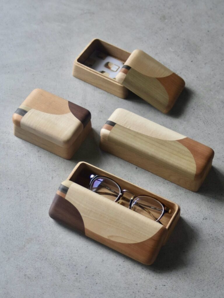 Handcrafted wooden boxes with curved lids and eyeglasses in one, on grey concrete.