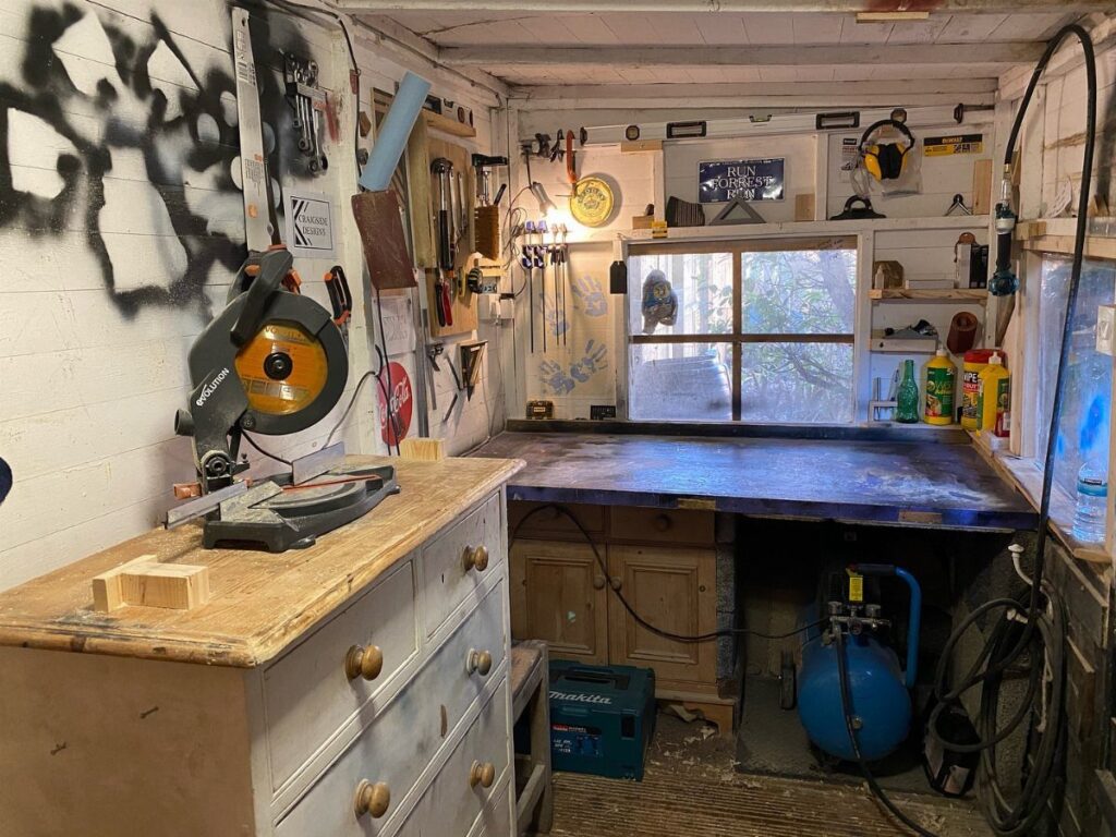 Small woodworking workshop with miter saw, air compressor, and tools on the walls.