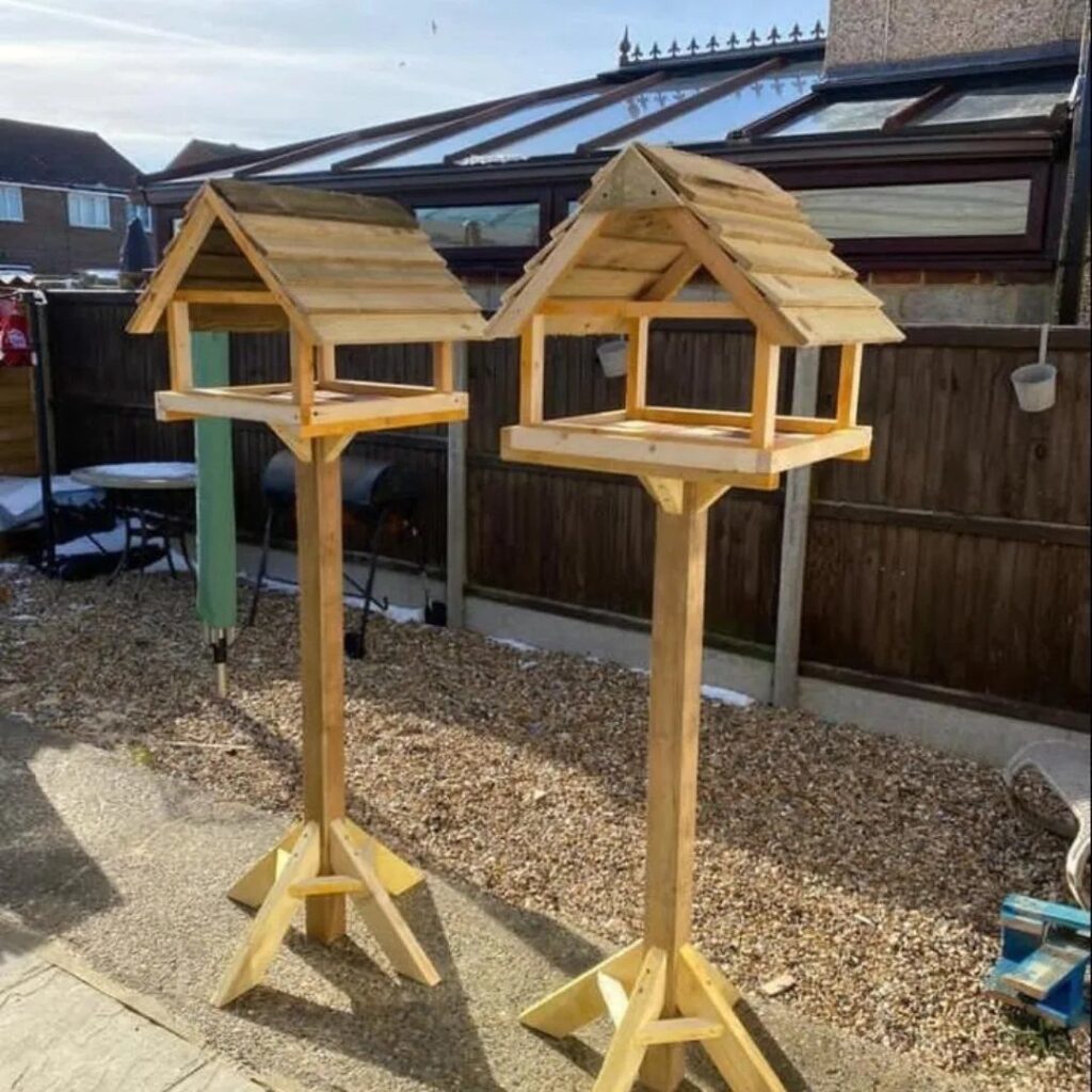 Two wooden birdhouses on tall posts standing in a backyard near a fence.