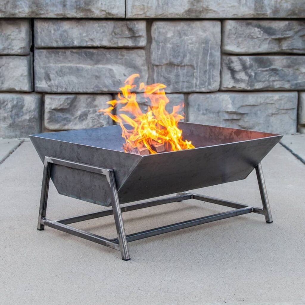 Square metal fire pit with burning orange flames on a concrete patio