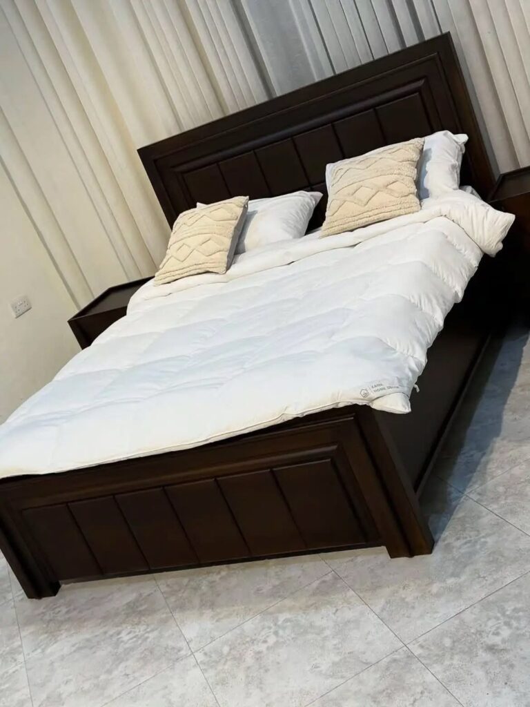 Dark brown wooden bed frame with white bedding and a paneled headboard.