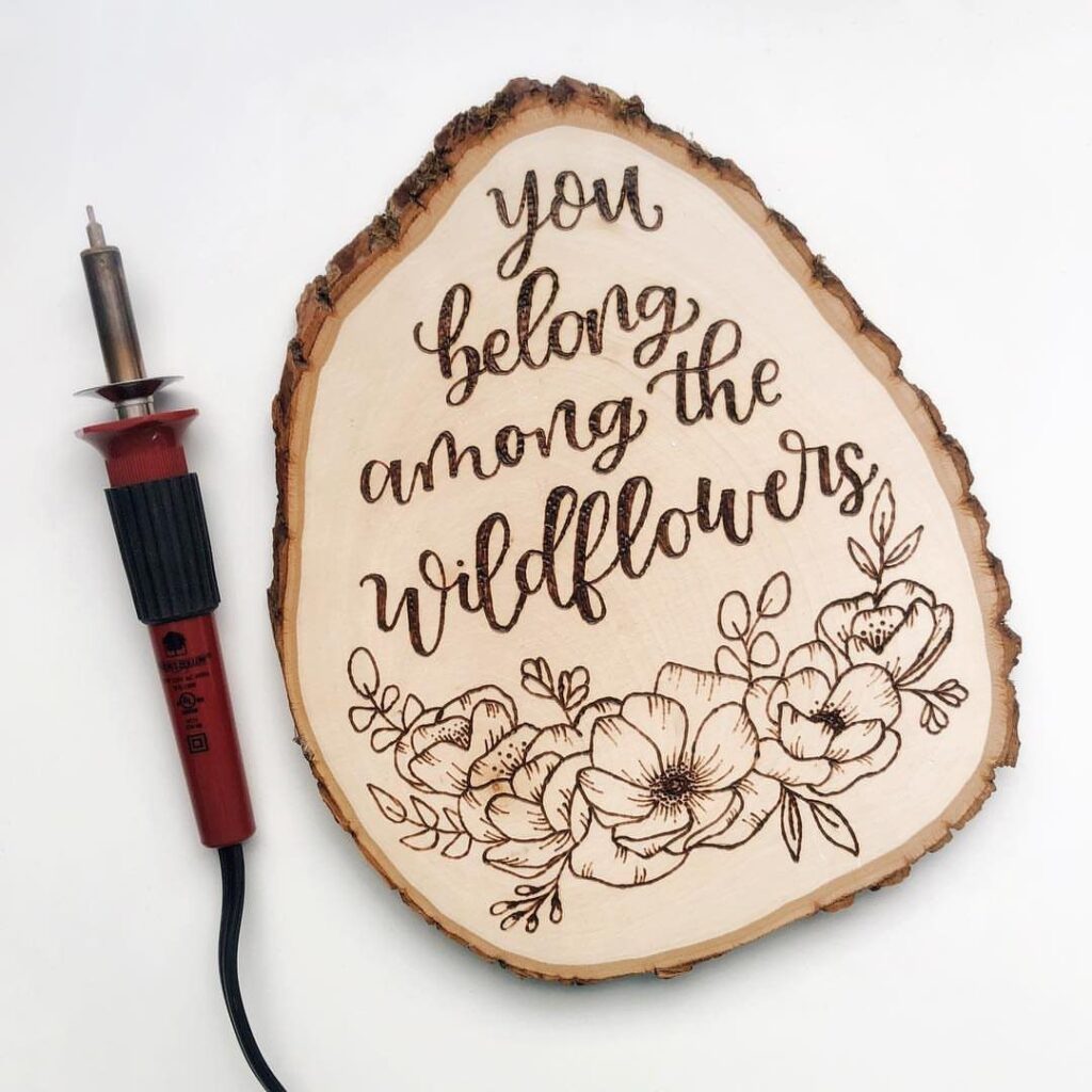 Wood burning tool and a wood slice with floral art and inspirational quote.
