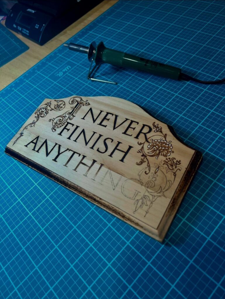 Wooden plaque with burned lettering and floral designs next to a wood-burning tool.
