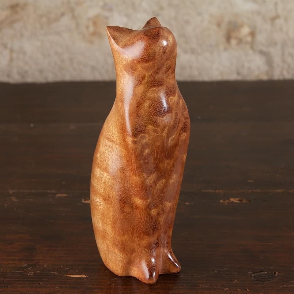 Polished wooden cat figurine with smooth curves standing on a dark wood table.