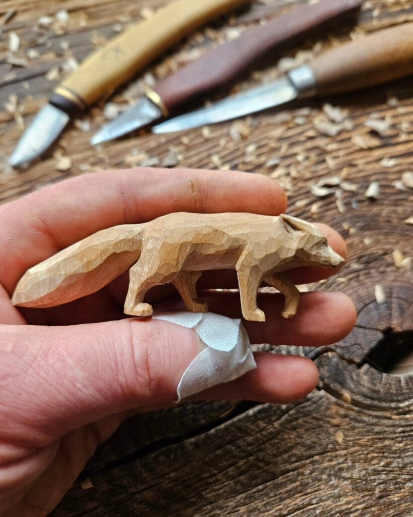 Small wooden fox carving held in a hand with carving tools nearby