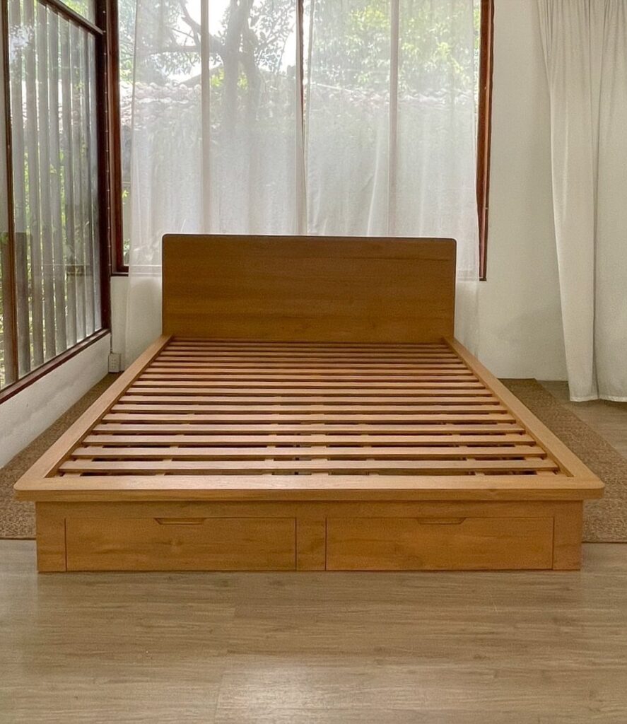 Wooden bed frame with a headboard, slatted base, and storage drawers in a bright room.