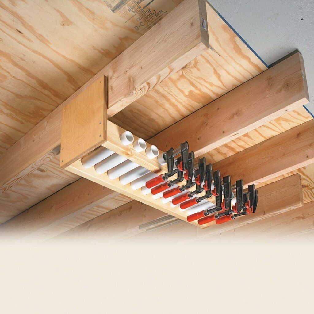 Wooden ceiling rack holding red and black bar clamps and white PVC pipes.