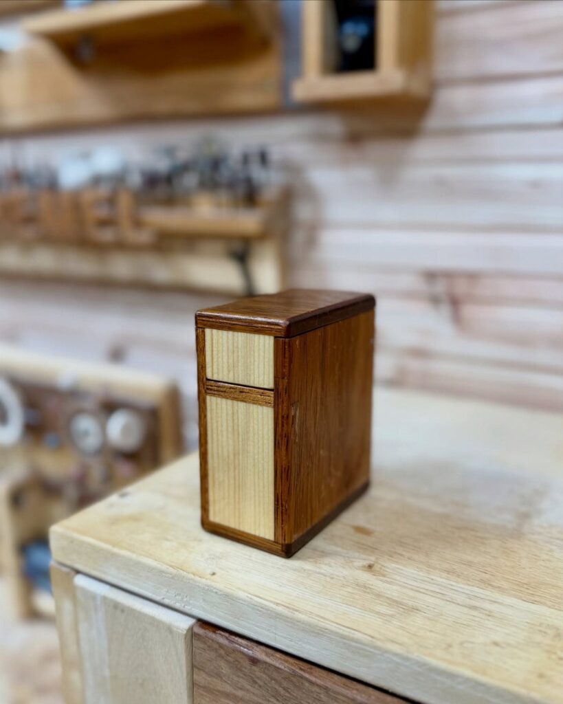 Small rectangular wooden box with light front panel on a workshop workbench.