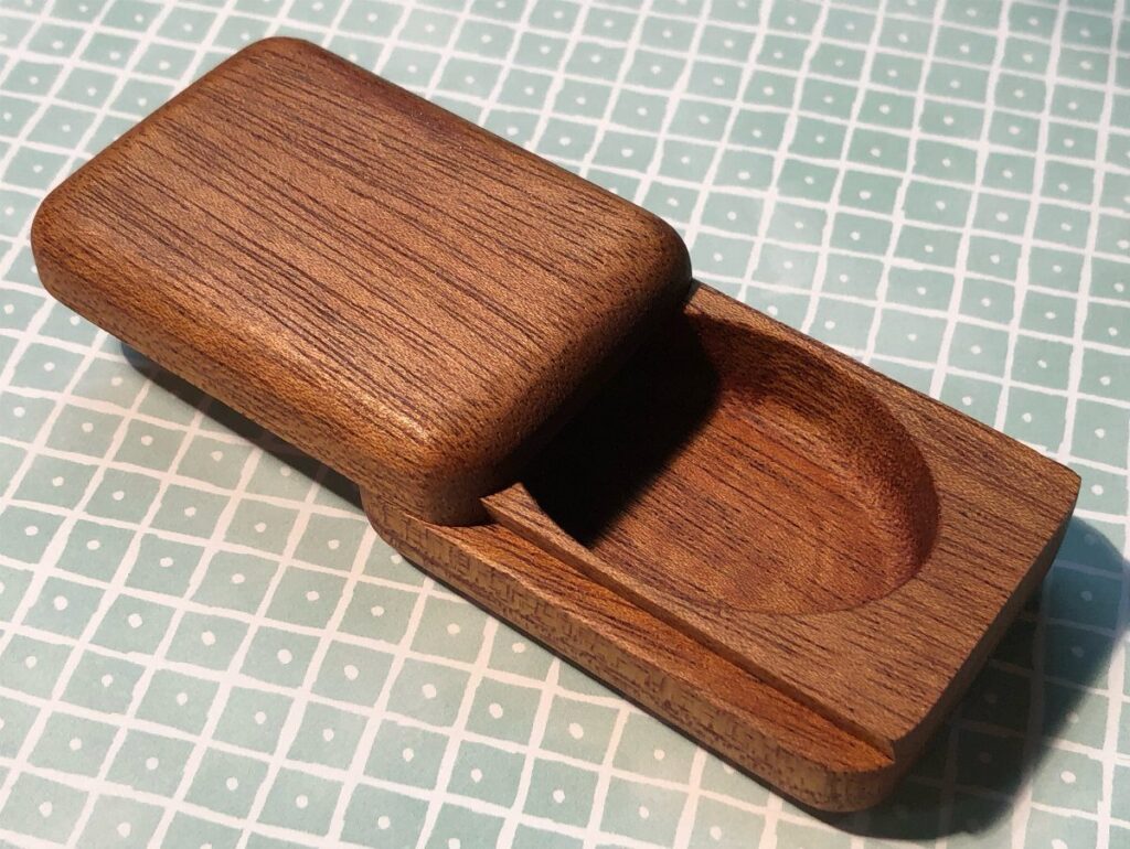 Small brown wooden box with a sliding lid open on a grid background